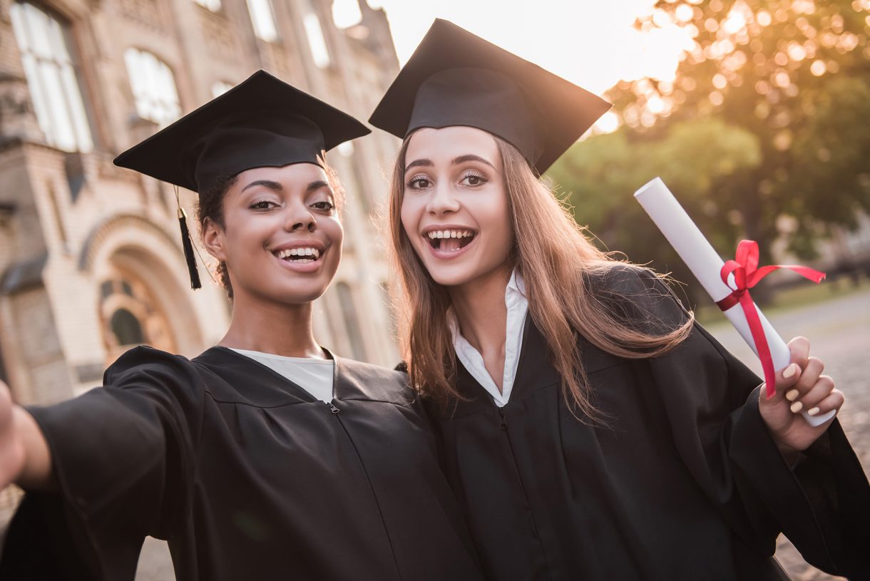 Photo of two young women college graduates in robes holding degrees