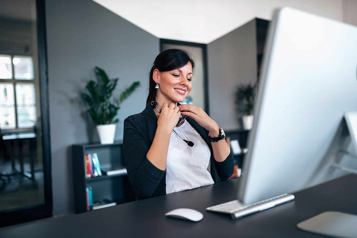 Smiling woman in front of computer with headphones hanging around neck