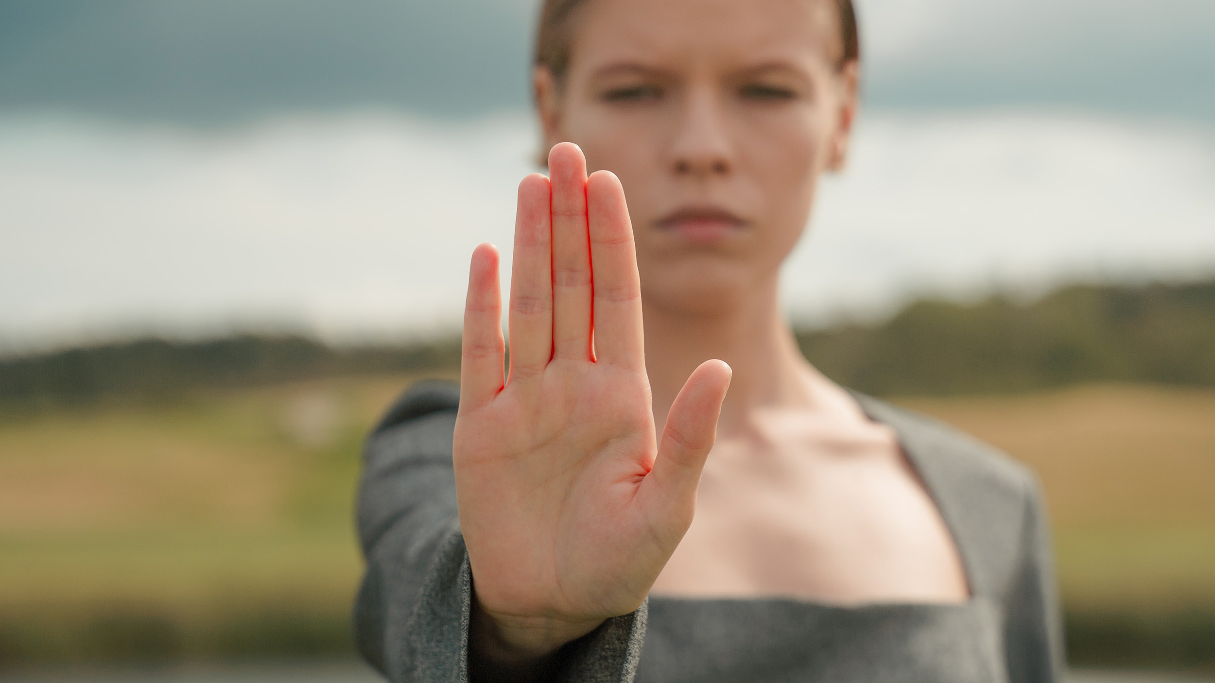 Closeup photo of young woman standing in field with her hand up motioning to stop