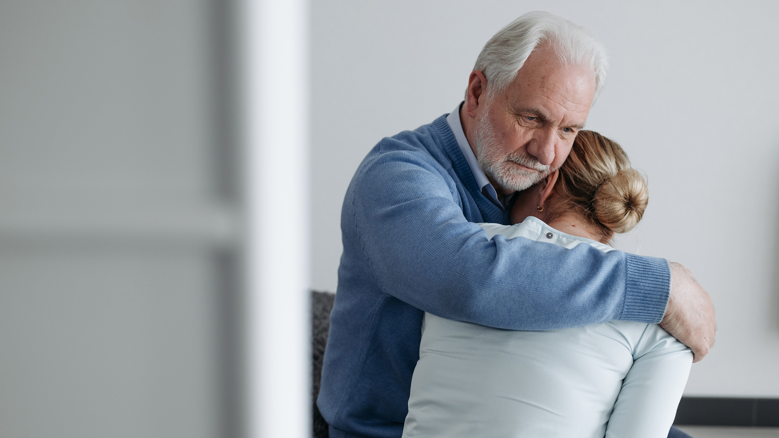 Photo of grief stricken elderly man hugging a younger woman